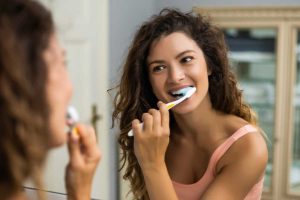 Woman with braces brushing teeth in front of a mirror.